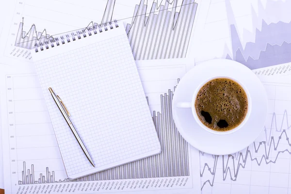 Cup of coffee, notepad and graphs — Stock Photo, Image