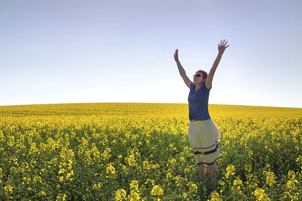 Mutlu kız mavi gökyüzünün altında kanola bitkiler arasında — Stok fotoğraf