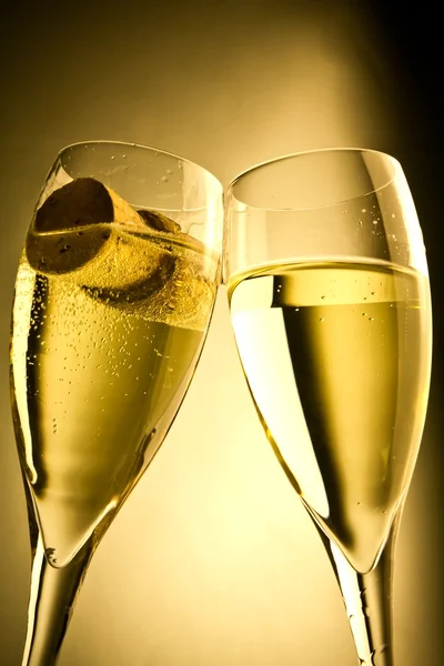 Een paar van champagne fluiten met fles dop tegen een gouden achtergrond — Stockfoto