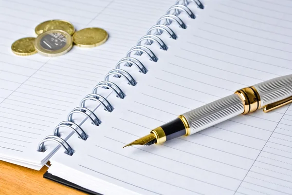 Bolígrafo de tinta en cuaderno y moneda fuera de foco —  Fotos de Stock