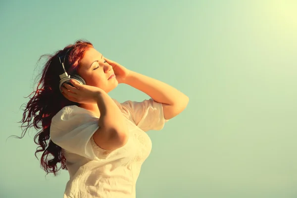 Gyönyörű vörös hajú lány hosszú haj élvezi a zenét a headphon — Stock Fotó