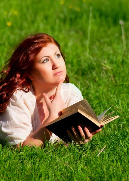 Рыжая красивая девушка читает книгу на природе — стоковое фото