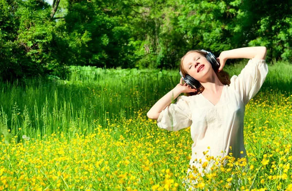 Beautiful girl in headphones enjoying the music in a field of fl — Stock Photo, Image