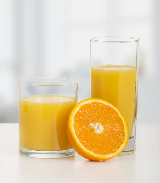 Два бокала апельсинового сока и нарезанный спелый апельсин — стоковое фото