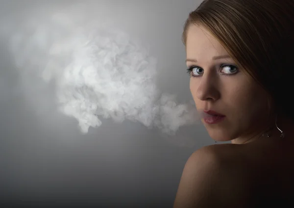 Красива молода жінка з сигаретним димом на темно-сірому фоні — стокове фото