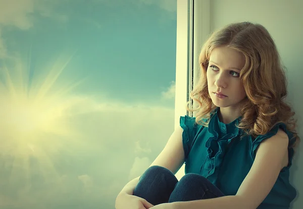 Грустная, красивая молодая женщина, тоскующая у окна на закате — стоковое фото