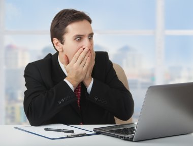 Surprised frightened businessman looking at a laptop, his han clipart