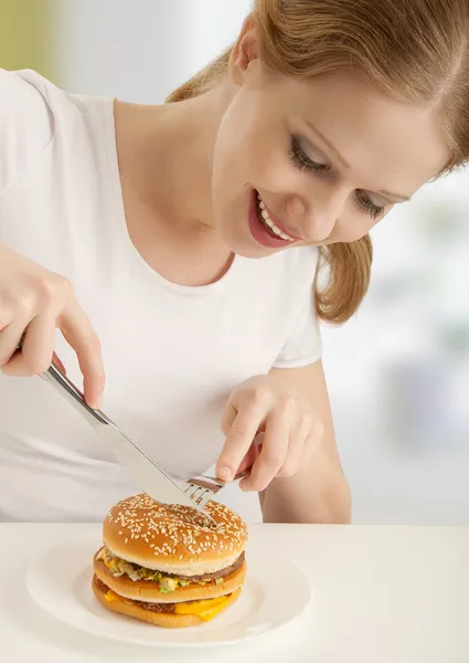 Atrakcyjna dziewczyna z widelcem i nożem zżera hamburgerów — Zdjęcie stockowe