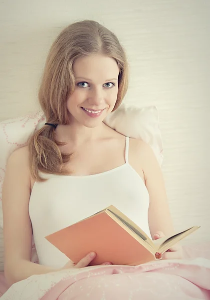 Bella ragazza bionda sta riposando a letto, leggendo un libro — Foto Stock