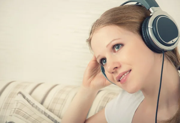 Beautiful girl enjoys listening to music on headphones on the so — Stock Photo, Image