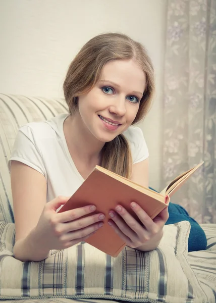 Όμορφο κορίτσι, διαβάζοντας ένα βιβλίο που βρίσκεται στον καναπέ — Φωτογραφία Αρχείου