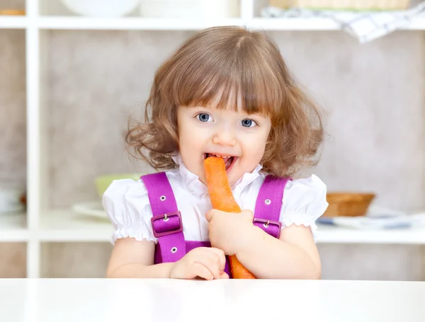 Niña comiendo zanahorias en la cocina — Foto de Stock