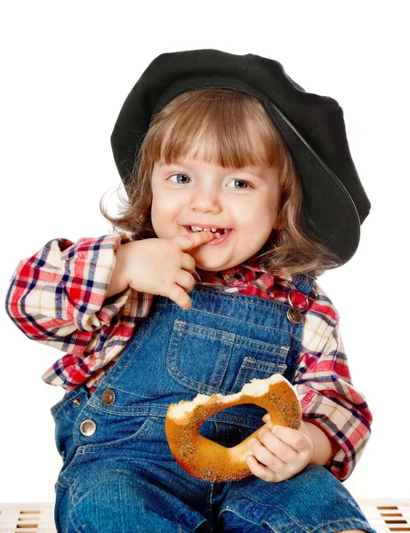 A beautiful little baby in a cap eating a loaf of bread — Stock Photo, Image