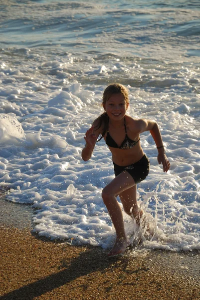 stock image Happy girl running away from the breaking waves.