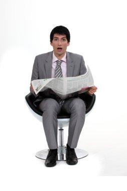 A dumbfounded businessman reading the newspaper. clipart