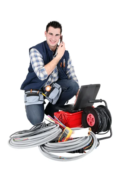 Eletricista fazendo uma chamada enquanto ajoelhado por seu equipamento — Fotografia de Stock