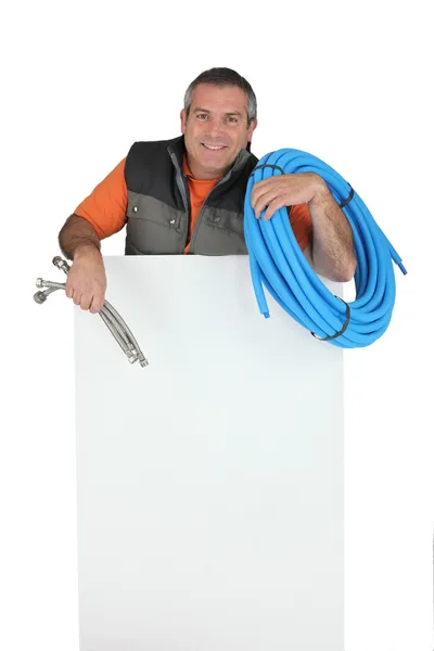 Plumber with materials and a board left blank for your message — Stock Photo, Image
