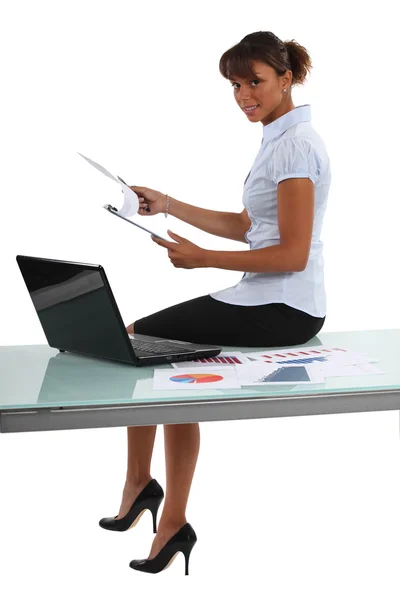 Businesswoman perched on a desk with statistics — Stock Photo, Image