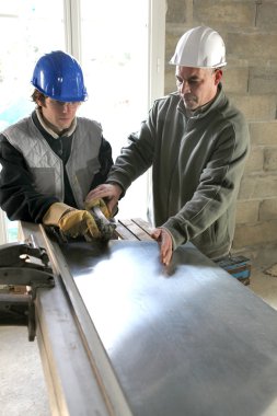 Apprentice being shown how to cut sheet metal clipart