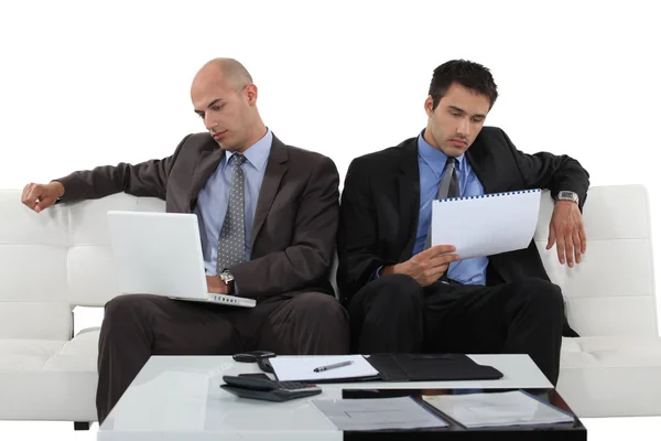 Due uomini d'affari seduti sul divano a controllare attraverso il documento — Foto Stock