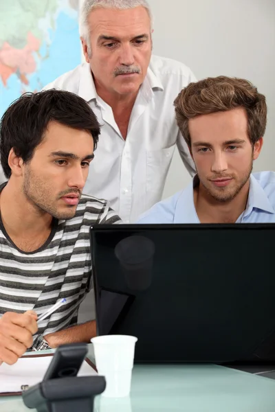 Männer sitzen um einen Laptop herum — Stockfoto