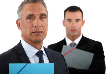 Portrait of a businessman with his assistant trailing behind him clipart