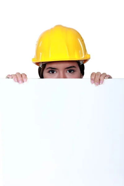 Een vrouwelijke bouwvakker verstopt achter een billboard. — Stockfoto