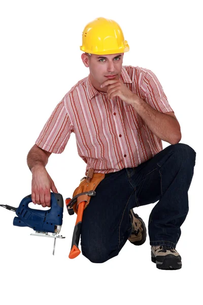 Уверенный рабочий, стоящий на коленях с бензопилой — стоковое фото