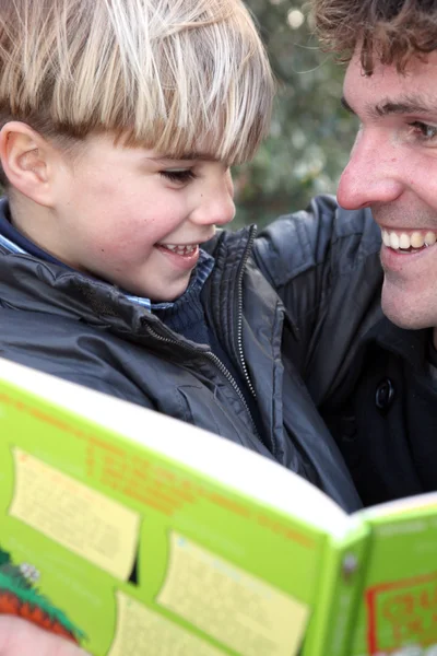 Чоловік з маленьким хлопчиком читає книгу на відкритому повітрі — стокове фото