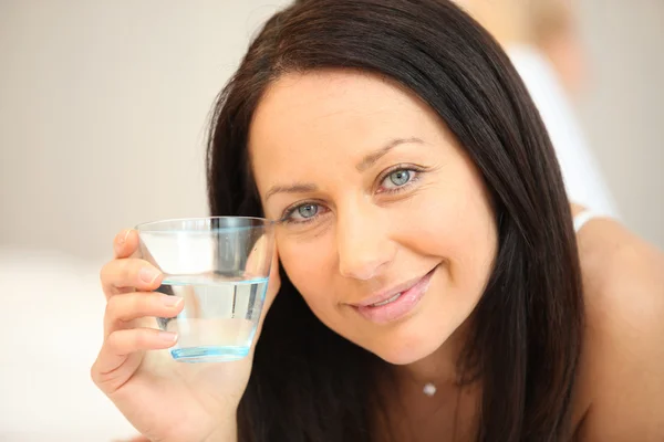 Bruna posa sul letto con un bicchiere d'acqua — Foto Stock