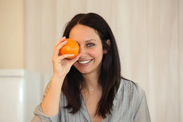 Mujer sosteniendo una naranja en su ojo — Foto de Stock