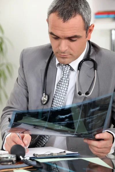 Doctor tomando notas escritas mientras examina la imagen de rayos X — Foto de Stock