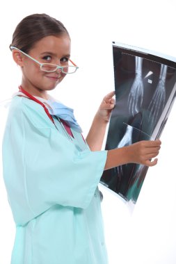 Little girl wearing hospital scrubs and examining an xray clipart