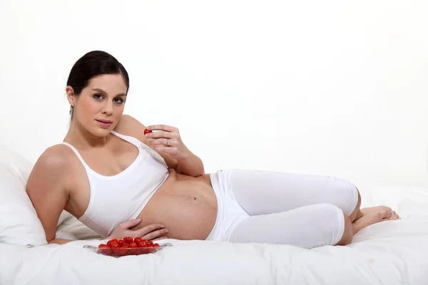 Mulher grávida deitada na cama comendo morangos — Fotografia de Stock