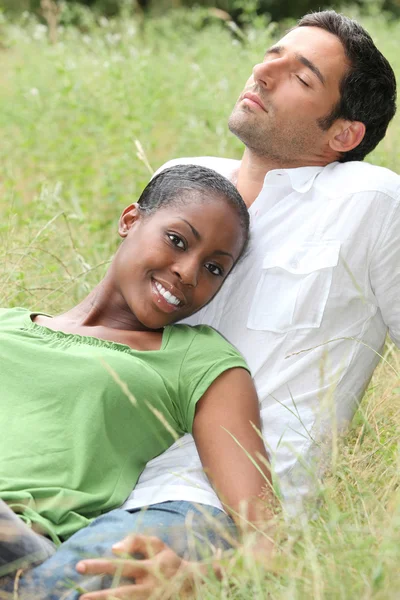 Mixed couple laying in a field — Stock Photo, Image
