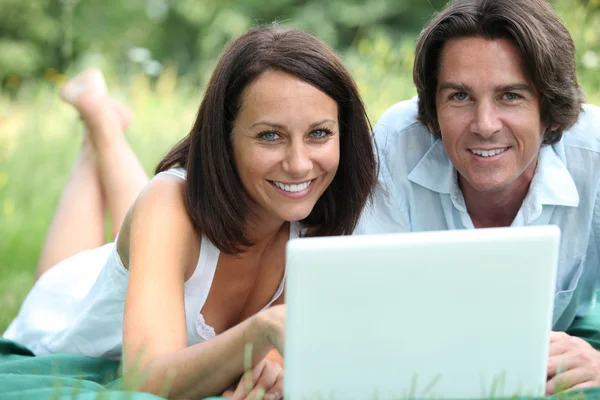 Couple with computer lying in the grass — Stock Photo, Image