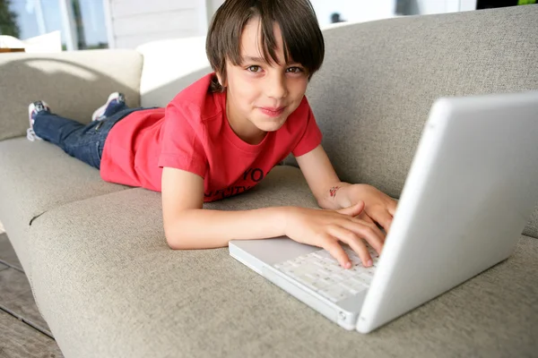 Jongen met behulp van een laptop op een sofa — Stockfoto
