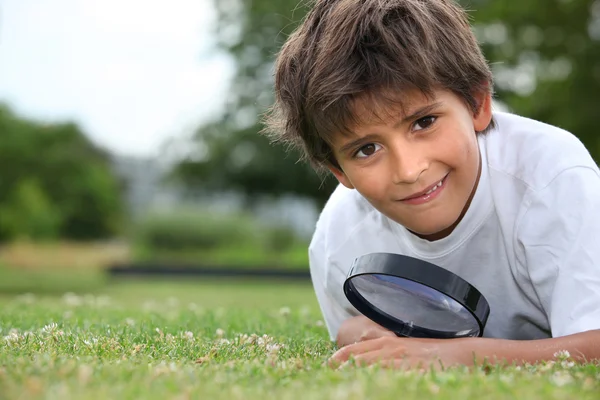 Хлопчик зі збільшувальним склом лежить на траві — стокове фото