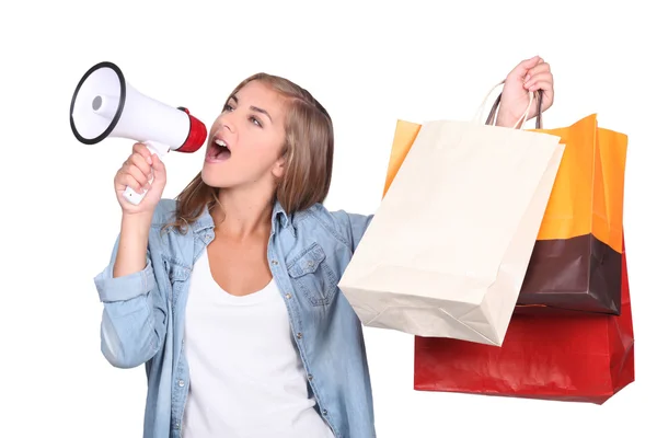 Studio shot of woman shouting into a megaphone and holding up store bags — Stock Photo, Image