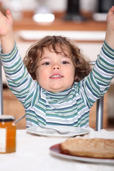 Маленький мальчик сидит за столом и перекусывает. — стоковое фото