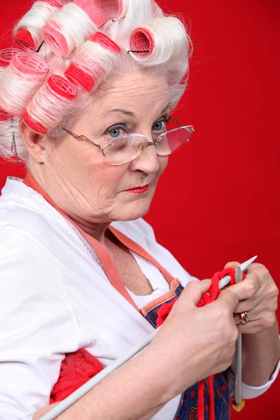 Old lady wearing hair rollers and knitting — Stock Photo, Image