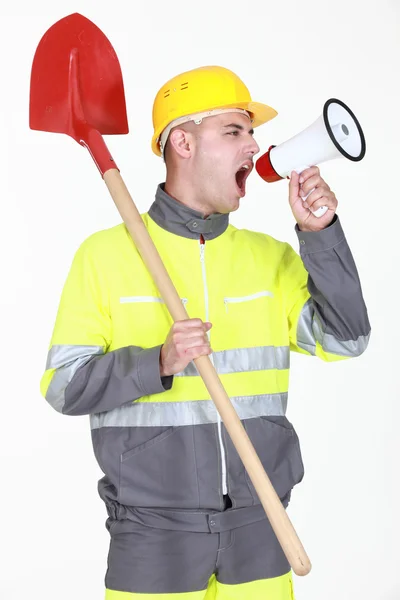 Construction with shovel shouting into megaphone — Stock Photo, Image