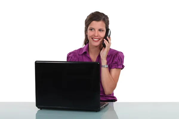 Молодая женщина за столом с ноутбуком и телефоном — стоковое фото