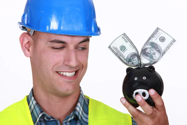 Stavební dělník s penězi v bance prasátko — Stock fotografie