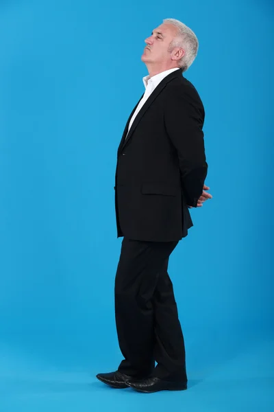 Hombre de mediana edad de pie con los brazos detrás de la espalda aislados en azul — Foto de Stock