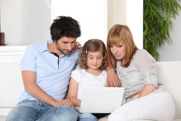 Família jovem reunida no sofá com laptop — Fotografia de Stock