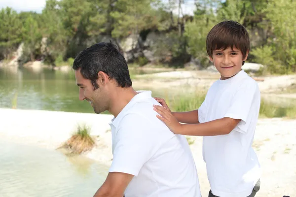 Niño empujando a su padre al borde de un río —  Fotos de Stock