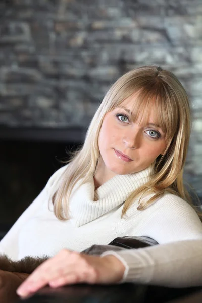 Woman sitting on a sofa in front of a fireplace — Stock Photo, Image