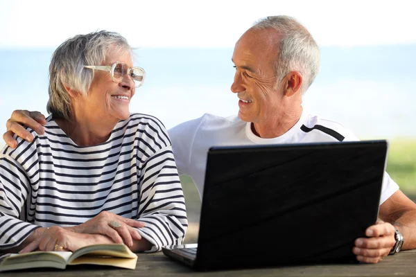Äldre par i trädgården med laptop och bok — Stockfoto