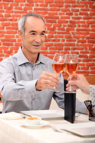 Äldre man höja ett glas i en restaurang — Stockfoto